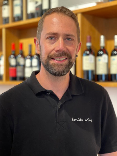 Person vor Weinflaschen im Regal.