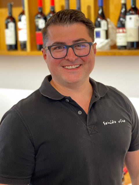 Mann vor Weinflaschen im Regal.